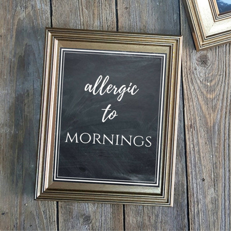"Allergic to Mornings" printable wall art featuring a rustic chalkboard design, perfect for farmhouse or modern decor. This digital download showcases a stylish combination of cursive and serif fonts in white text on a black.