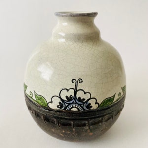 May include: A small, round, white ceramic vase with a crackled glaze. It has a brown base with a decorative band and a floral design in green, blue, and black.