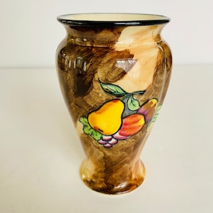 May include: A brown and cream ceramic vase with a black rim. The vase features a fruit design with a pear, grapes, and other fruits in shades of yellow, red, and purple.
