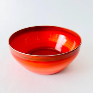 Op de afbeelding: Een feloranje kom met een zilveren rand en subtiele oranje en bruine strepen. De kom is gemaakt van een glanzend materiaal en is perfect om snacks of salades in te serveren.