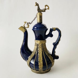May include: A blue ceramic teapot with gold accents and a bird finial on the lid. The teapot has a spout and a handle.