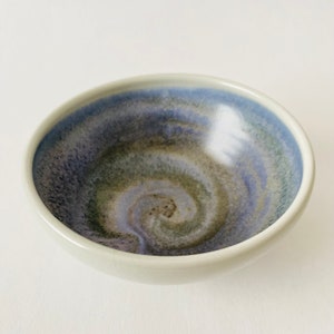 Op de afbeelding: Een kleine, witte keramische kom met een blauwe, groene en paarse swirl-patroon erin.