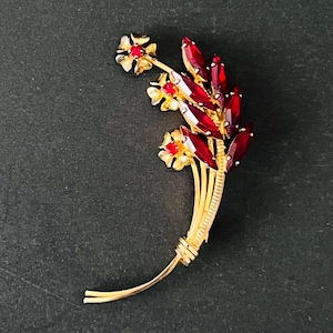 Op de afbeelding: Goudkleurige broche in de vorm van een bloemenboeket. De broche heeft rode edelsteenaccenten en kleine gouden bloemen met rode centra. Het ontwerp is gedetailleerd en elegant, met een klassieke vintage esthetiek.