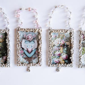 May include: Four silver-toned frames with ornate edges, each containing a different vintage-style image of a cross and flowers. Each frame is hung from a beaded chain with a crystal pendant.