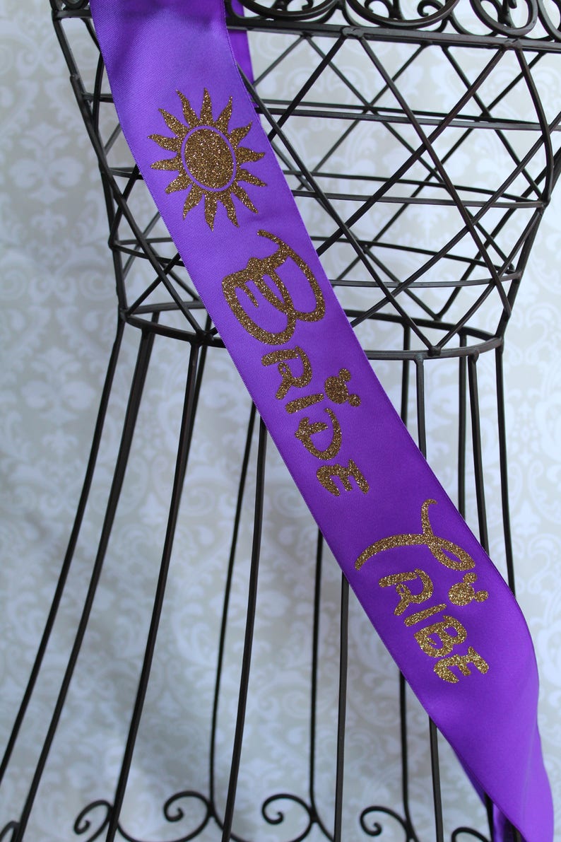 Puede incluir: Banda de sat&eacute;n morado con letras doradas de purpurina que dicen "Bride to Be" y un dise&ntilde;o de sol de purpurina dorada.