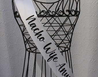 May include: White satin sash with black text that reads "Nacho Wife Anymore". The sash is draped over a black metal dress form.