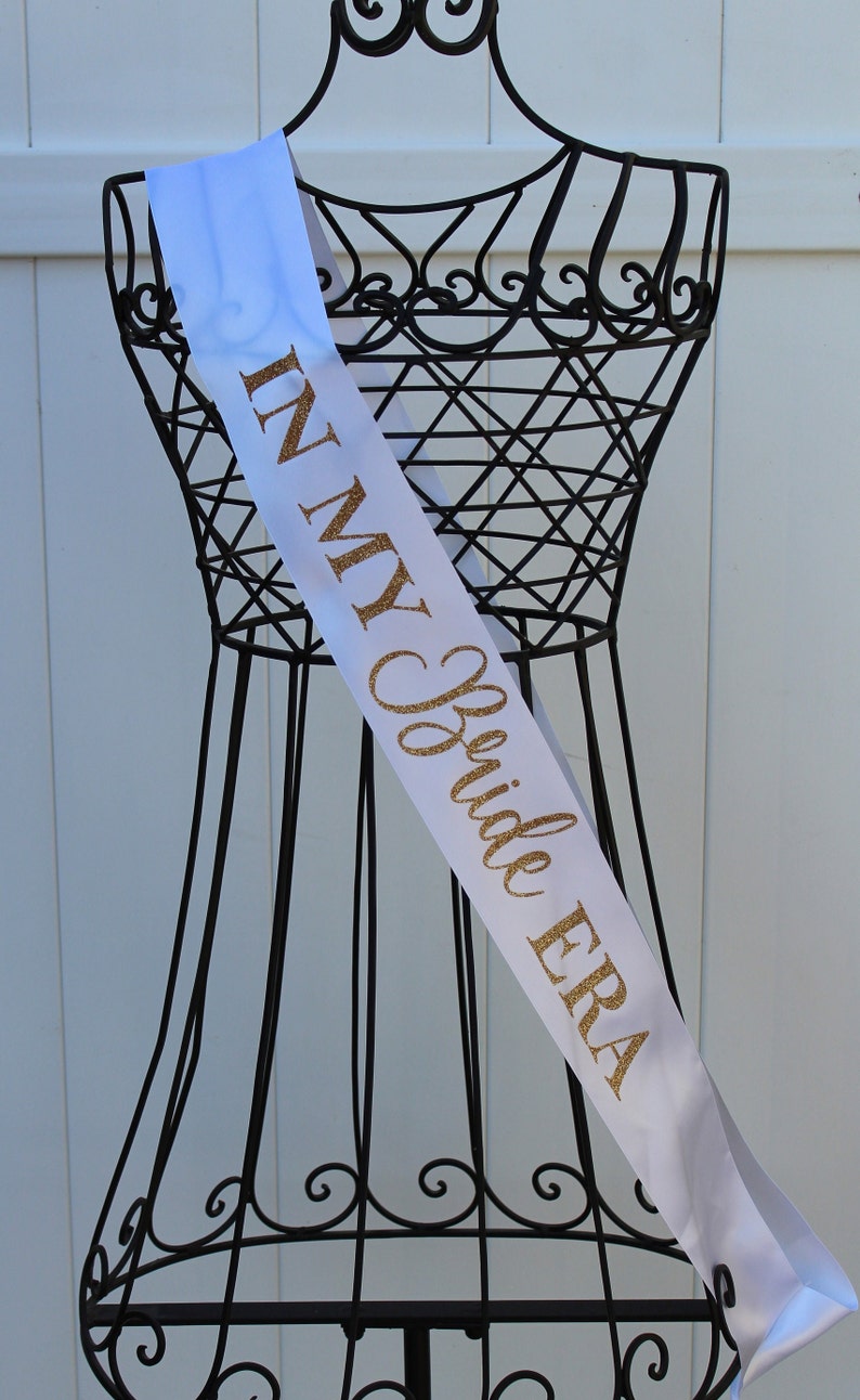May include: White satin sash with gold glitter lettering that reads "In My Bride Era".