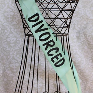 May include: A mint green satin sash with the word "DIVORCED" printed in black glitter.