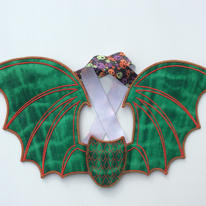 May include: Green dragon wings with red stitching and gold trim. The wings are attached to a white ribbon with a skull and crossbones pattern.