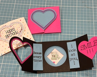 May include: Three handmade greeting cards with different designs. The first card is pink with a blue heart cutout. The second card is black with a pink heart cutout and a blue background with the text "Because every time". The third card is black with a blue background and the text "I look at you, I" and a pink heart cutout with the text "SMILE!!!".