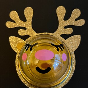 Peut inclure: Une d&eacute;coration de renne en paillettes dor&eacute;es avec un d&ocirc;me en plastique transparent et un visage de dessin anim&eacute; mignon. Le renne a des joues roses, des cils noirs et un sourire noir.
