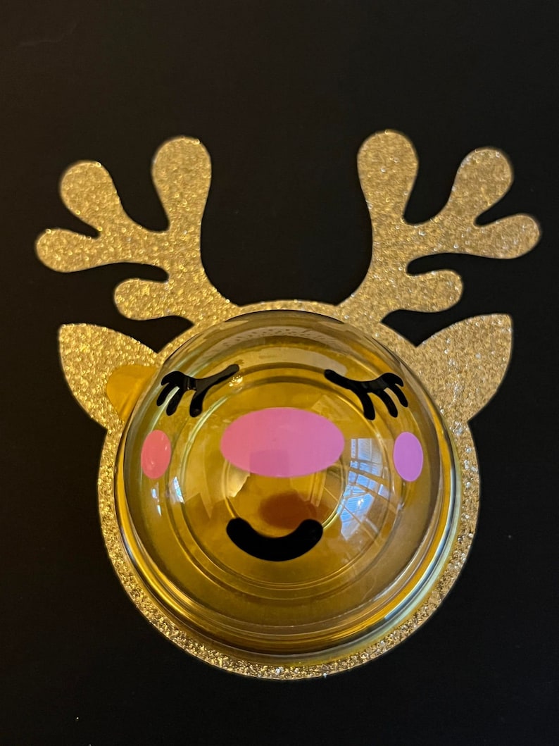 Peut inclure: Une d&eacute;coration de renne en paillettes dor&eacute;es avec un d&ocirc;me en plastique transparent et un visage de dessin anim&eacute; mignon. Le renne a des joues roses, des cils noirs et un sourire noir.