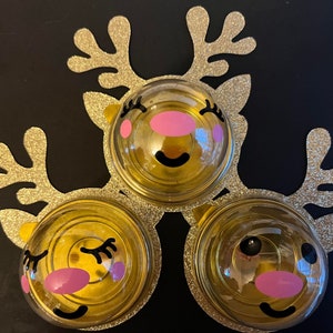 Peut inclure: Trois d&eacute;corations de rennes dor&eacute;es avec des accents de paillettes. Chaque d&eacute;coration a un d&ocirc;me en plastique transparent avec un visage de renne de dessin anim&eacute; mignon avec des joues roses et des yeux noirs.