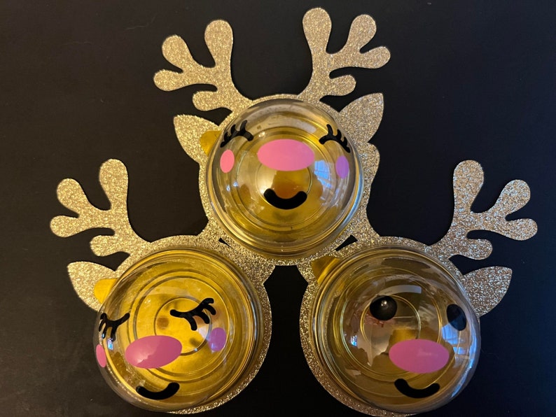 Peut inclure: Trois d&eacute;corations de rennes dor&eacute;es avec des accents de paillettes. Chaque d&eacute;coration a un d&ocirc;me en plastique transparent avec un visage de renne de dessin anim&eacute; mignon avec des joues roses et des yeux noirs.