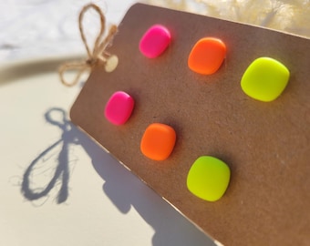 May include: A close-up of a brown tag with six colorful, neon-colored stud earrings. The earrings are in shades of pink, orange, and yellow-green. The tag is tied with a natural twine bow.