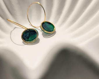 May include: A pair of hoop earrings featuring circular pendants with a deep emerald green marbled finish encased in thin gold-toned metal rims. The earrings have slender gold-toned wires that extend from the top of the circular pendants.