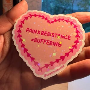 May include: A heart-shaped sticker with a holographic finish featuring a pink background, a dark pink scalloped border with heart accents, and the text "PAIN X RESISTANCE = SUFFERING" in dark pink, along with the handle @sarahtoninbooost.