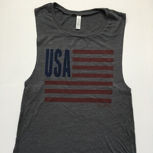 K&ouml;nnte beinhalten: Ein graues &auml;rmelloses Tanktop mit einem rot-wei&szlig;-blauen amerikanischen Flaggen-Motiv und dem Text "USA" in Blau. Der Text "Est. 1976" ist in Rot unter der Flagge gedruckt.