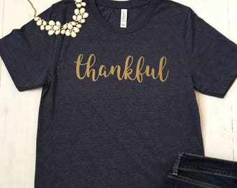 May include: A dark blue t-shirt with the word "thankful" written in gold lettering.