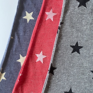 May include: Three fabric swatches with different colored backgrounds and star patterns. The first swatch is a dark blue fabric with white stars. The second swatch is a bright red fabric with white stars. The third swatch is a gray fabric with black stars.