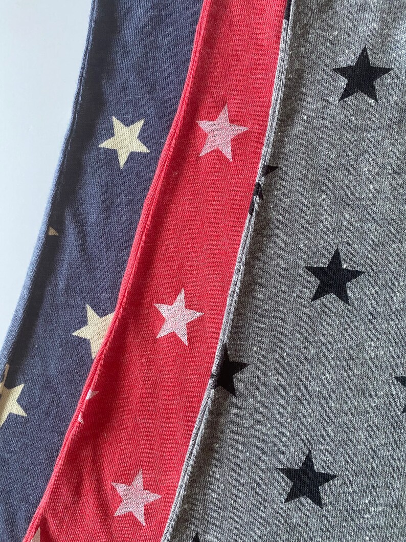 May include: Three fabric swatches with different colored backgrounds and star patterns. The first swatch is a dark blue fabric with white stars. The second swatch is a bright red fabric with white stars. The third swatch is a gray fabric with black stars.