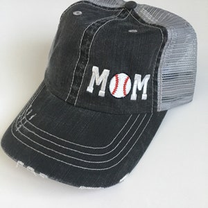 May include: A black and grey baseball cap with a distressed look. The front of the cap has the word "MOM" embroidered in white with a red and white baseball in the "O".