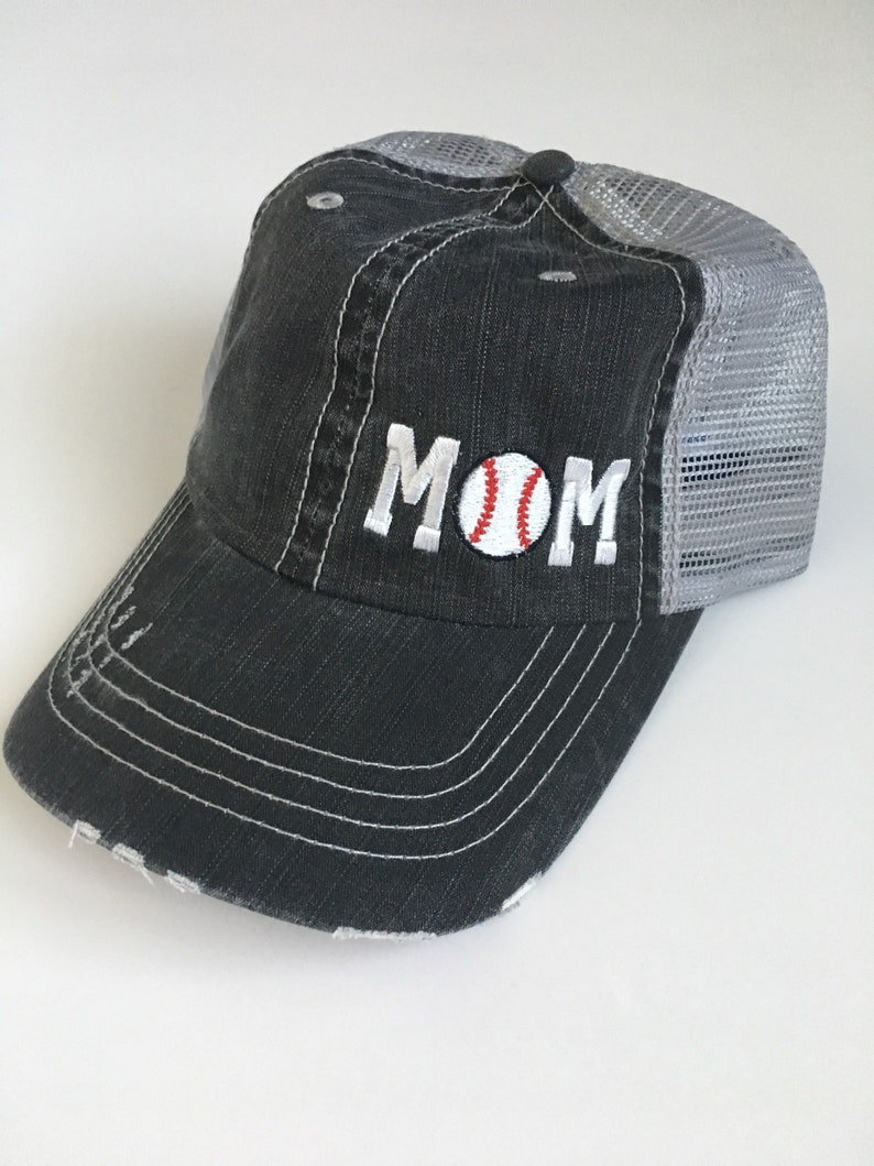 May include: A black and grey baseball cap with a distressed look. The front of the cap has the word "MOM" embroidered in white with a red and white baseball in the "O".