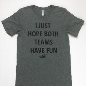 May include: A heather gray t-shirt with the text "I just hope both teams have fun" printed in black. A small black and white illustration of a megaphone with the text "Go Team" is below the text.
