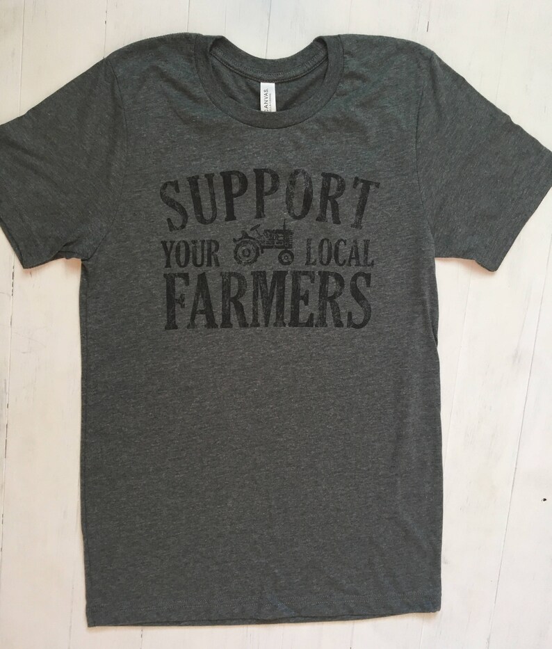 May include: A dark grey t-shirt with the text "Support Your Local Farmers" printed in black. A small tractor graphic is included in the text.