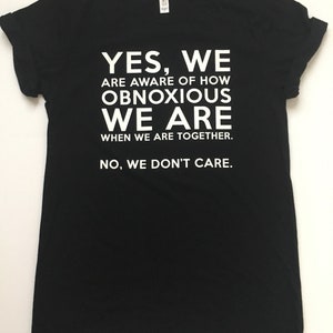 Może przedstawiać: Czarny T-shirt z białym tekstem, kt&oacute;ry brzmi: "YES, WE ARE AWARE OF HOW OBNOXIOUS WE ARE WHEN WE ARE TOGETHER. NO, WE DON'T CARE."
