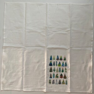 K&ouml;nnte beinhalten: Ein wei&szlig;es Geschirrtuch mit einem Muster aus bunten Weihnachtsb&auml;umen. Die B&auml;ume sind in verschiedenen Gr&uuml;nt&ouml;nen, Blau- und Rott&ouml;nen gehalten.