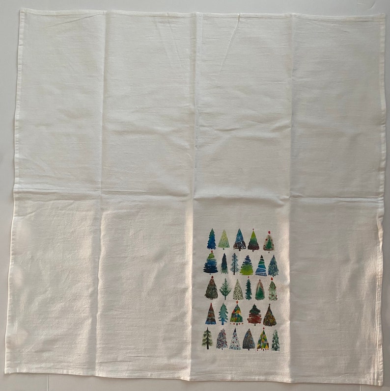 K&ouml;nnte beinhalten: Ein wei&szlig;es Geschirrtuch mit einem Muster aus bunten Weihnachtsb&auml;umen. Die B&auml;ume sind in verschiedenen Gr&uuml;nt&ouml;nen, Blau- und Rott&ouml;nen gehalten.