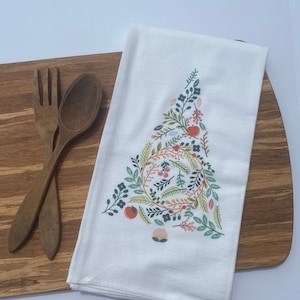 Könnte beinhalten: Ein weißes Geschirrtuch mit einem floralen Muster in Grün-, Blau-, Rosa- und Orangetönen. Das Muster ist ein stilisierter Baum mit Blättern, Blüten und Beeren.