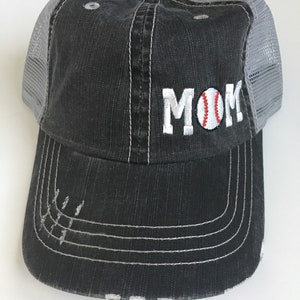 May include: A black and grey baseball cap with a mesh back. The front of the cap has the word "MOM" embroidered in white with a baseball graphic in the "O".