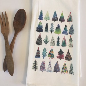 K&ouml;nnte beinhalten: Ein wei&szlig;es Geschirrtuch mit einem farbenfrohen Aquarelldesign aus verschiedenen Weihnachtsb&auml;umen. Die B&auml;ume sind in Blaut&ouml;nen, Gr&uuml;n, Rot und Gelb gemalt.