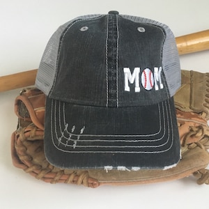 May include: A black and grey baseball cap with a white mesh back. The cap has the word "MOM" embroidered on the front with a baseball in the "O".