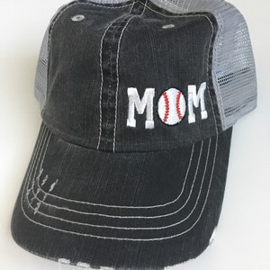 May include: Black and grey baseball cap with a white embroidered baseball and the word "MOM" on the front.