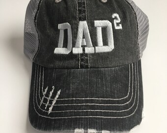 Könnte beinhalten: Eine schwarze und graue, abgenutzte Trucker-Kappe mit einem weißen gestickten Design, das "DAD²" sagt.