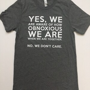 Może przedstawiać: Szary t-shirt z białym nadrukiem, kt&oacute;ry brzmi: "YES, WE ARE AWARE OF HOW OBNOXIOUS WE ARE WHEN WE ARE TOGETHER. NO, WE DON'T CARE."