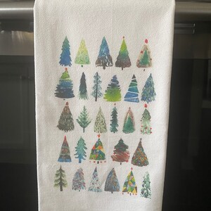 K&ouml;nnte beinhalten: Ein wei&szlig;es K&uuml;chentuch mit einem farbenfrohen Design aus 36 Weihnachtsb&auml;umen. Die B&auml;ume sind in verschiedenen Gr&uuml;nt&ouml;nen, Blau- und Rott&ouml;nen bemalt, einige mit geometrischen Mustern.