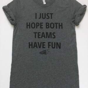 May include: A heather gray t-shirt with the text "I JUST HOPE BOTH TEAMS HAVE FUN" printed in black. A small black and white graphic of a megaphone with the text "GO TEAM" is below the text.