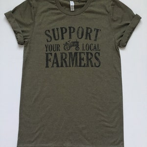 May include: A green t-shirt with the text "Support Your Local Farmers" in black lettering. A small black silhouette of a tractor is above the word "Local".