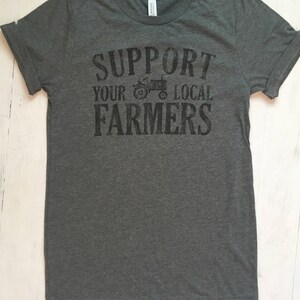 May include: A dark grey t-shirt with the text "Support Your Local Farmers" printed on the front. A small tractor graphic is included in the text.