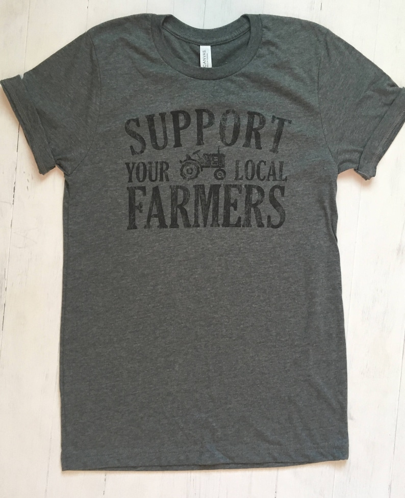 May include: A dark grey t-shirt with the text "Support Your Local Farmers" printed on the front. A small tractor graphic is included in the text.
