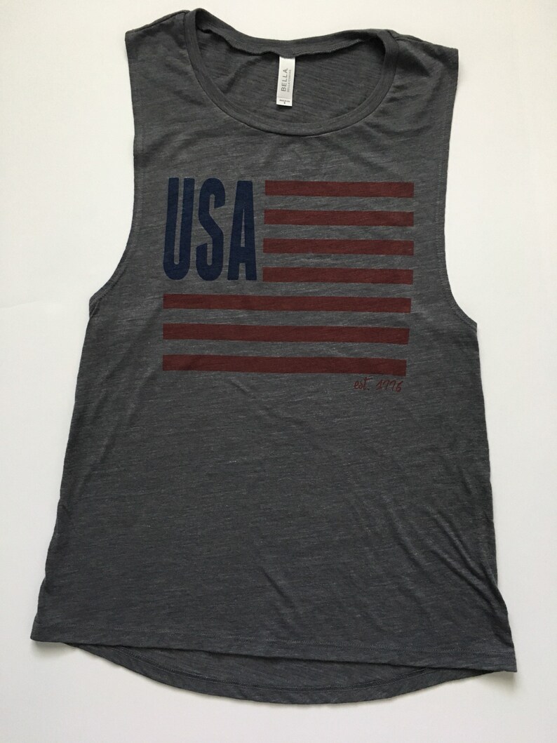 K&ouml;nnte beinhalten: Ein graues &auml;rmelloses Tanktop mit einem rot-wei&szlig;-blauen amerikanischen Flaggen-Motiv und dem Text "USA" in Blau. Der Text "Est. 1976" ist in Rot unter der Flagge gedruckt.