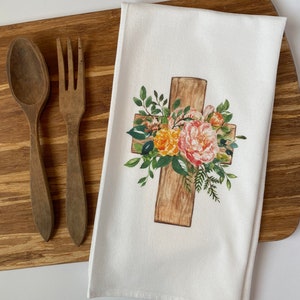 Könnte beinhalten: Ein weißes Küchentuch mit einem Blumendesign auf einem Holzkreuz. Die Blumen sind rosa, gelb und orange.