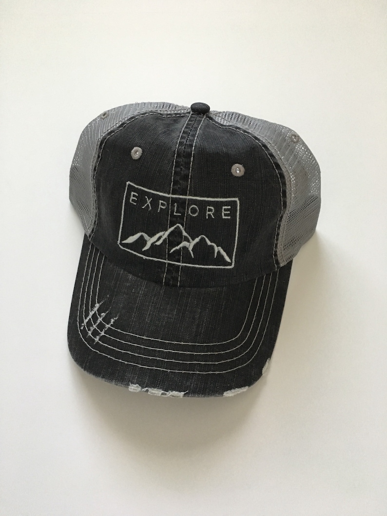 May include: A black and gray distressed trucker hat with a white embroidered mountain range and the word "EXPLORE" in a rectangle.