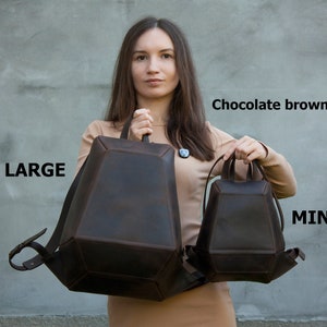 Puede incluir: Dos mochilas de cuero de color marrón chocolate. La mochila más grande está etiquetada como "LARGE" y la mochila más pequeña está etiquetada como "MINI".