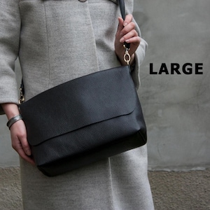 Puede incluir: Un bolso de hombro grande de cuero negro con cierre de solapa. El bolso tiene una correa larga y herrajes dorados. La palabra "LARGE" está impresa en negrita, en negro, en el lado derecho de la imagen.