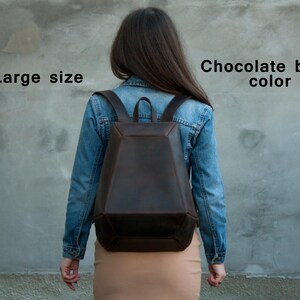 May include: A large, chocolate brown backpack with a geometric design. The backpack has adjustable straps and a top handle. The image shows the back of the backpack, worn by a person. The text on the image says "Large size" and "Chocolate brown color".
